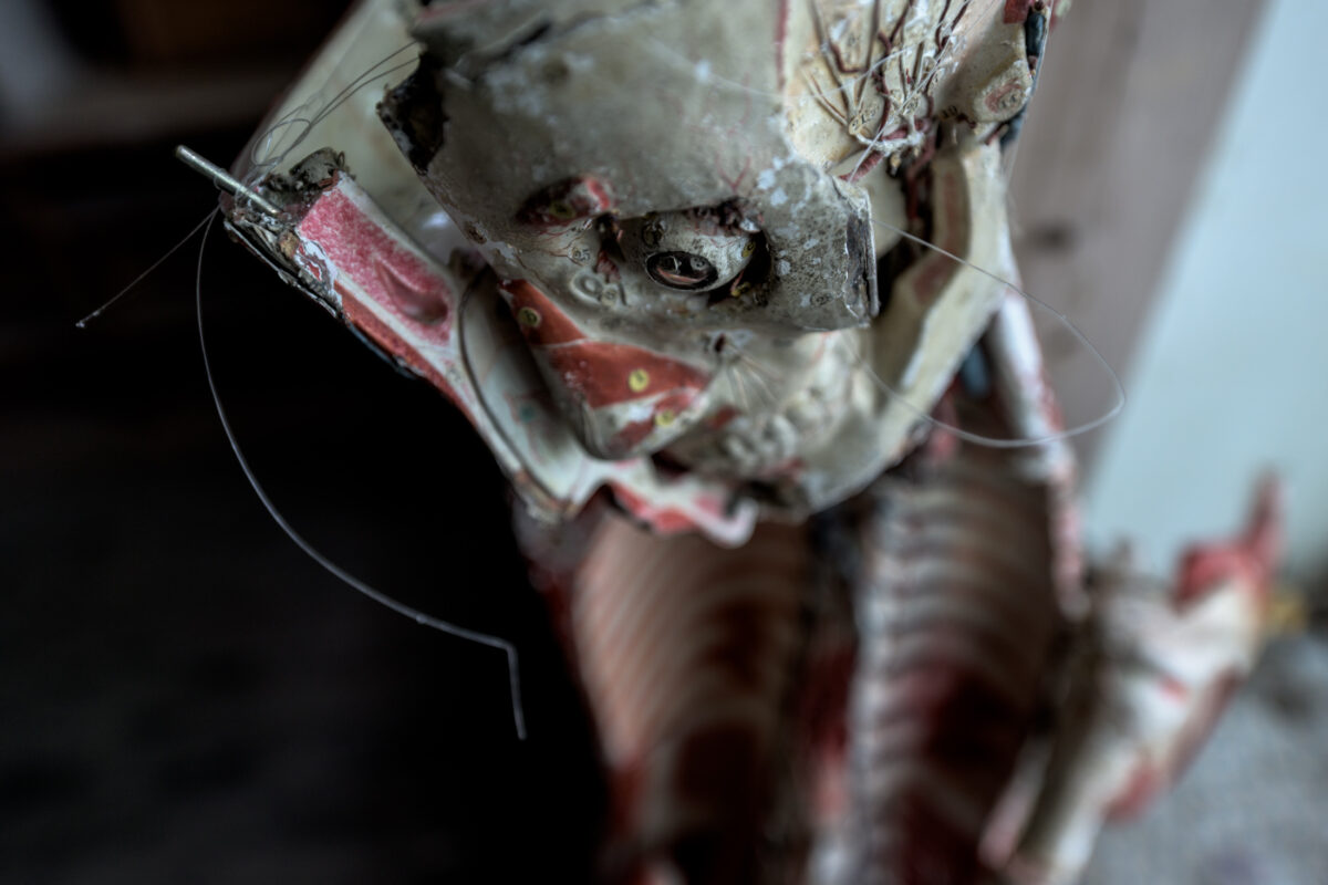 Creepy broken mannequin effigy with exposed wires in dark abandoned school hallway