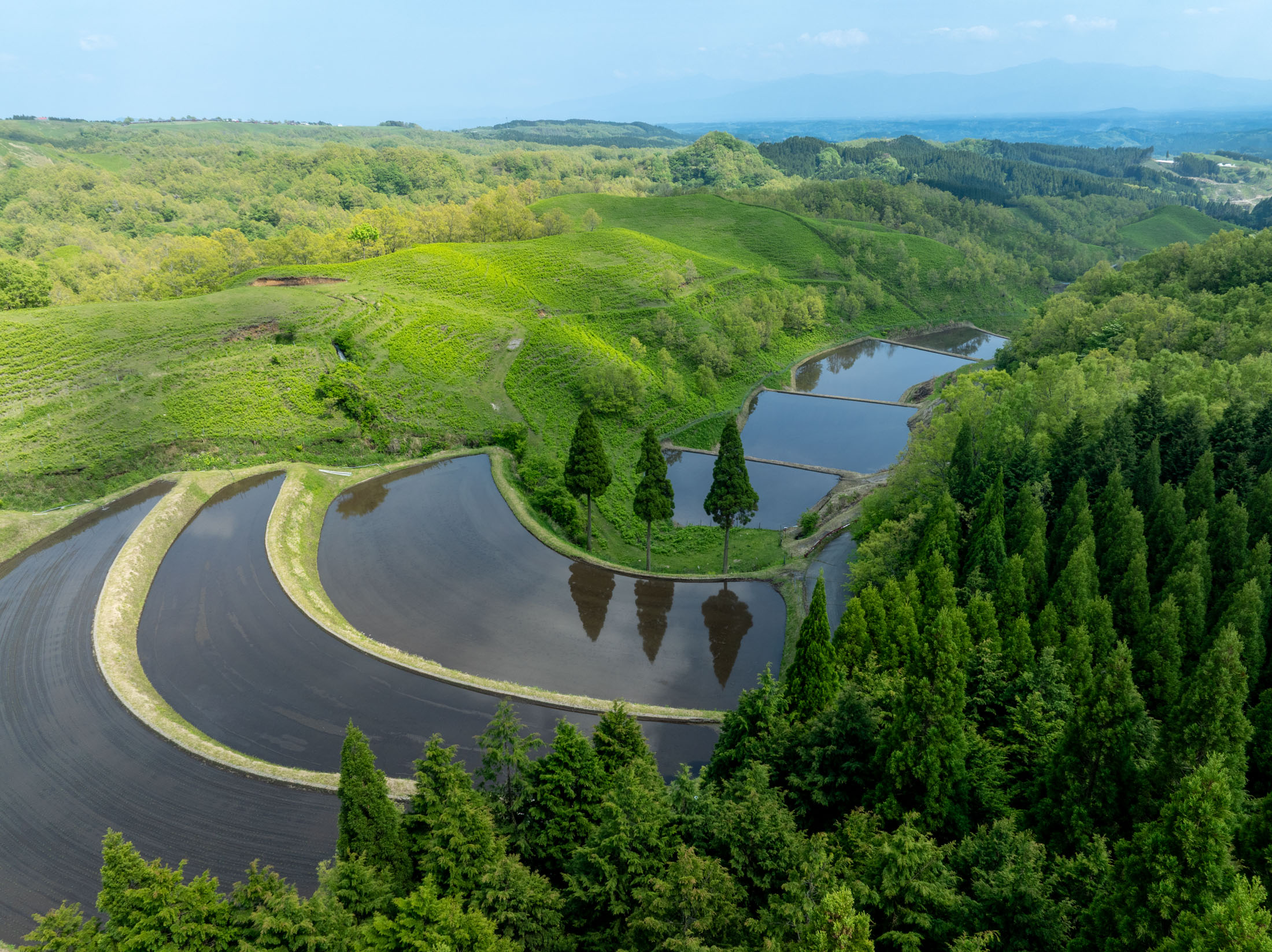 Aerial view of Ogi rice terraces with water-filled paddies reflecting sky on green hills